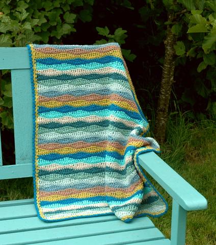 image shows a blanket in waves of blue and sand draped over a blue chair