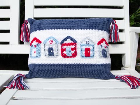 image shows a blue and white cushion with a row of blue, white and red beach huts in a nautical theme.