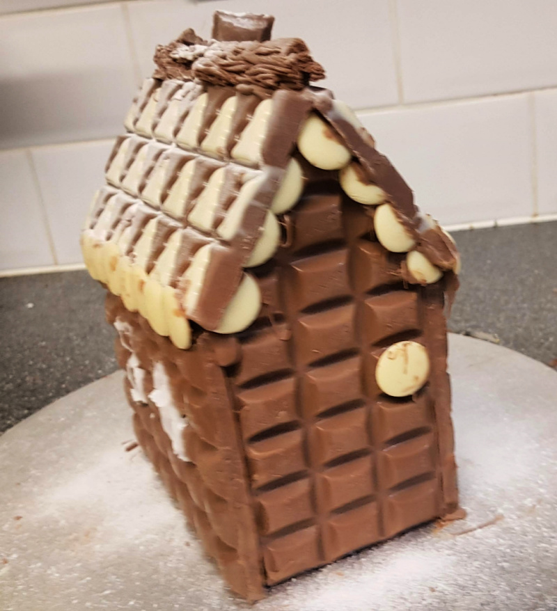 completed chocolate gingerbread house with roof and decorations
