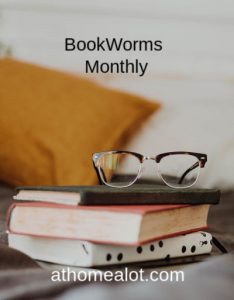 book worms monthly a pile of books at different angles with a pair of reading glasses on top and a cushion in the  background.